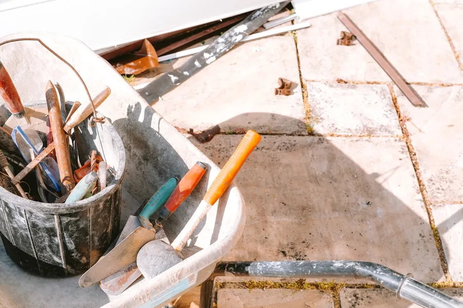 An assortment of hand tools in a wheelbarrow on a job site.